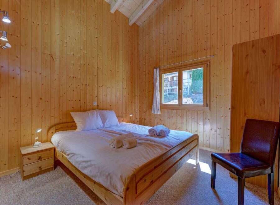 Experience cozy living in this charming wooden-paneled bedroom, featuring a comfortable queen-sized bed with crisp white linens and plush towels.