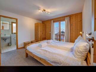 Experience cozy mountain living in this charming bedroom featuring a comfortable bed, ample wooden wardrobe, and a private balcony with stunning alpine views.