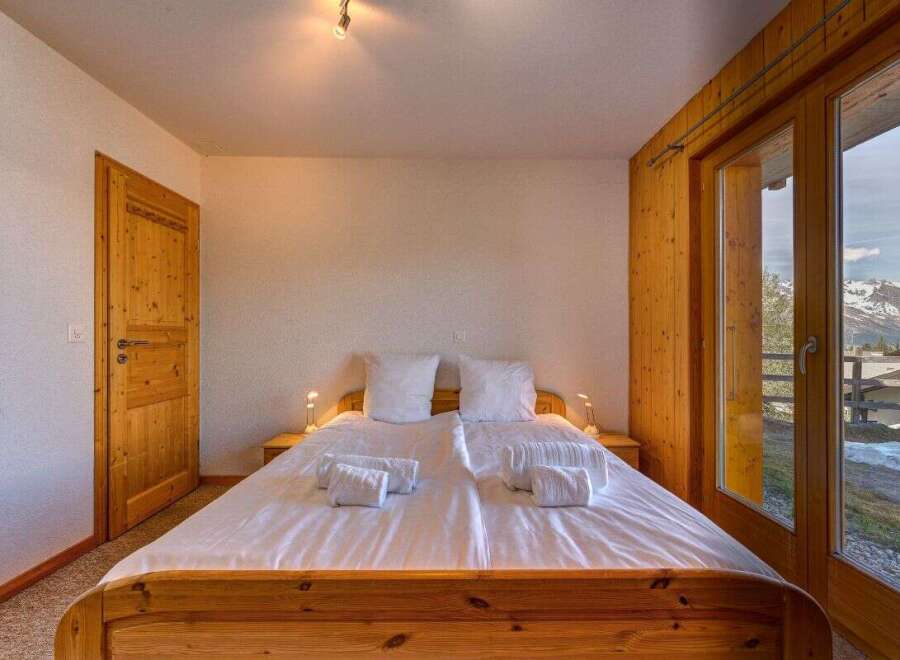 Experience breathtaking mountain views from this charming bedroom, featuring a comfortable double bed and a large glass door leading to a private balcony.