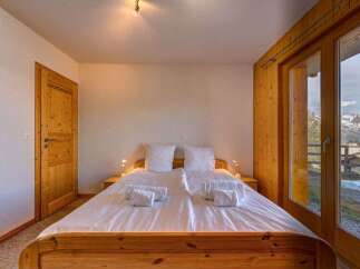 Experience breathtaking mountain views from this charming bedroom, featuring a comfortable double bed and a large glass door leading to a private balcony.