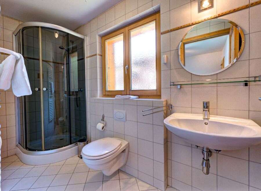 This charming bathroom features a modern glass-enclosed shower, a sleek wall-mounted toilet, and a stylish vanity with a large oval mirror.
