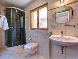 This charming bathroom features a modern glass-enclosed shower, a sleek wall-mounted toilet, and a stylish vanity with a large oval mirror.