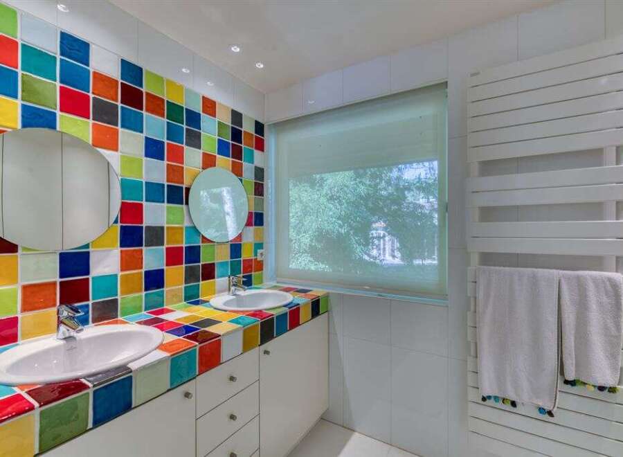 This vibrant bathroom features a unique design with colorful tiled walls and countertops, creating a cheerful and inviting atmosphere.