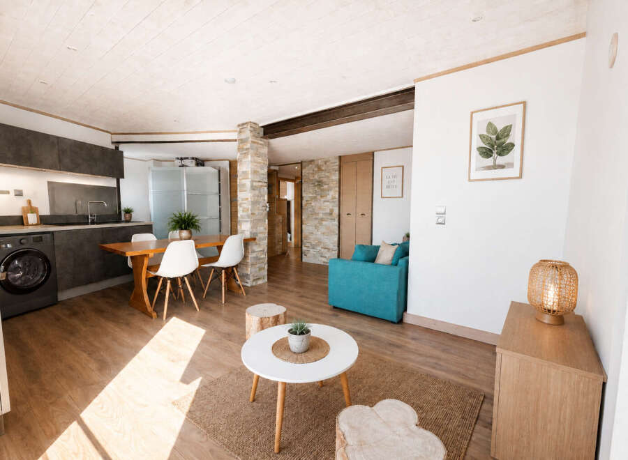 Discover this modern open-plan living space featuring a sleek kitchen with dark cabinetry and integrated appliances, adjacent to a dining area with a wooden table and white chairs.
