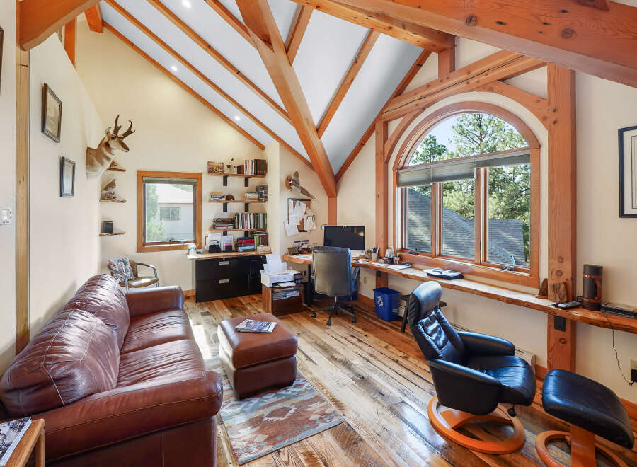 This stunning home office boasts a unique architectural design with exposed wooden beams and a vaulted ceiling, creating a warm and inviting atmosphere.