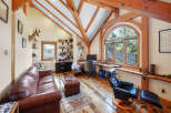 This stunning home office boasts a unique architectural design with exposed wooden beams and a vaulted ceiling, creating a warm and inviting atmosphere.