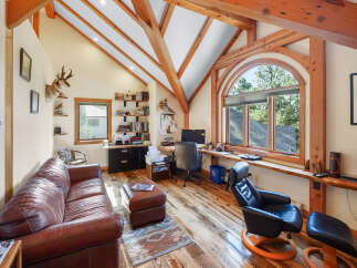 This stunning home office boasts a unique architectural design with exposed wooden beams and a vaulted ceiling, creating a warm and inviting atmosphere.