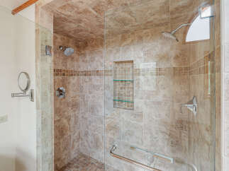 Experience luxury in this stunning bathroom featuring a spacious walk-in shower with elegant travertine tile and a convenient built-in niche with glass shelves.