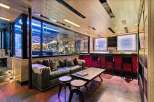 Experience ultimate luxury in this custom-designed entertainment space, featuring a stunning motorcycle display encased in glass, a plush leather sofa, and a fully equipped bar with plush red seating.