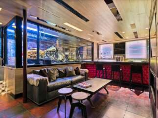 Experience ultimate luxury in this custom-designed entertainment space, featuring a stunning motorcycle display encased in glass, a plush leather sofa, and a fully equipped bar with plush red seating.