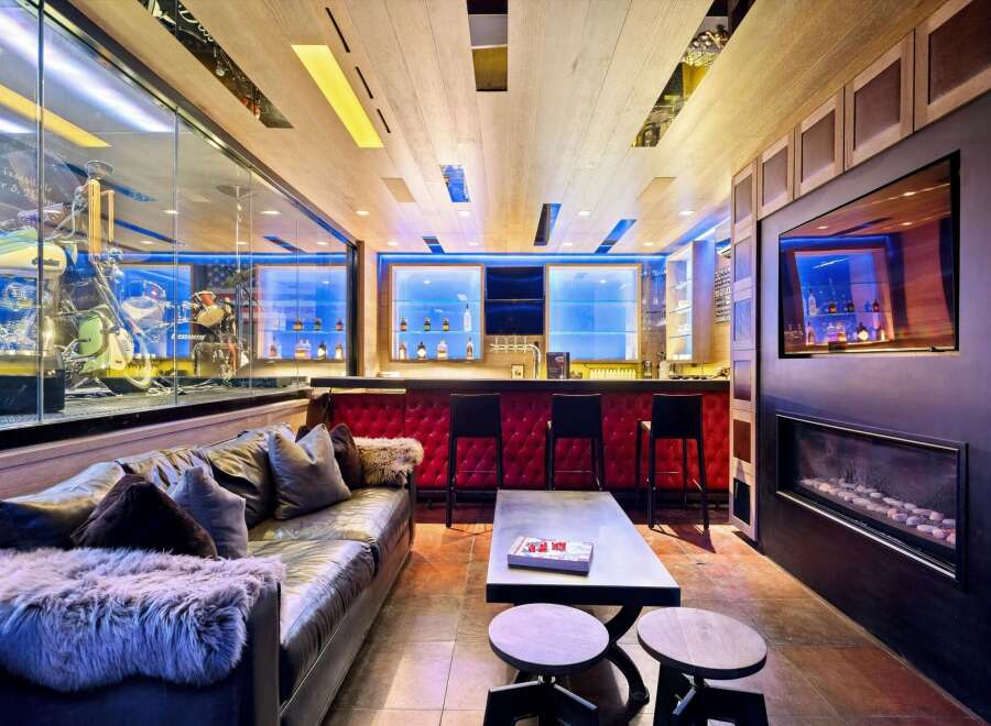 Experience ultimate luxury in this custom-designed entertainment space, featuring a stunning motorcycle display, a fully equipped bar with plush seating, and a modern fireplace.