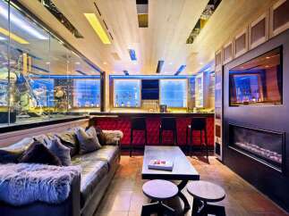 Experience ultimate luxury in this custom-designed entertainment space, featuring a stunning motorcycle display, a fully equipped bar with plush seating, and a modern fireplace.