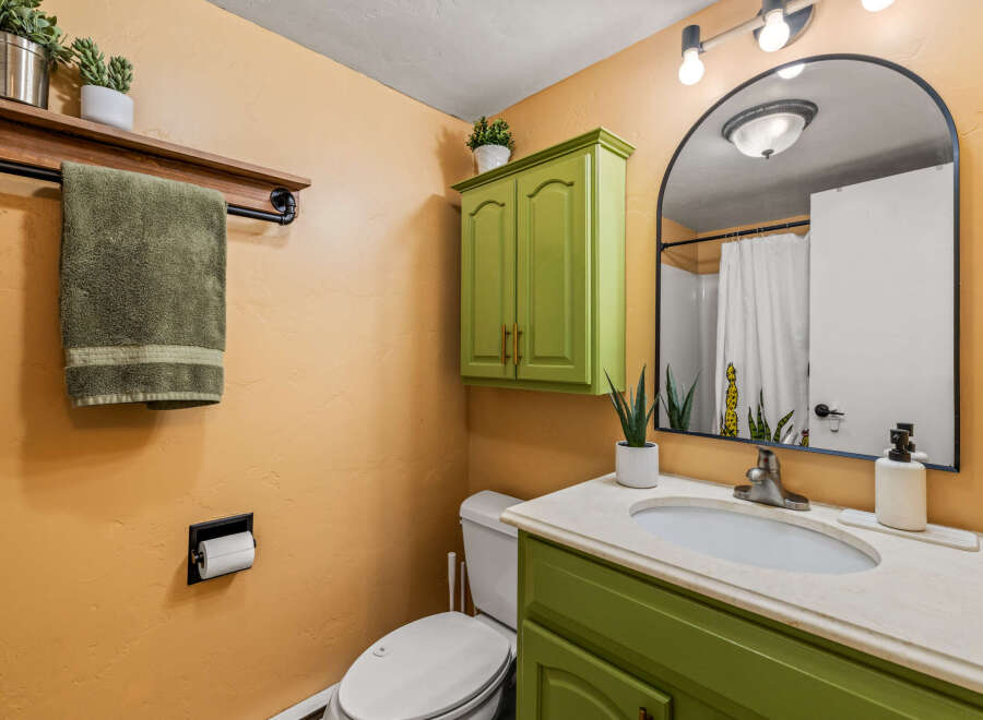 This charming bathroom features a unique green vanity and cabinet, adding a pop of color to the space.