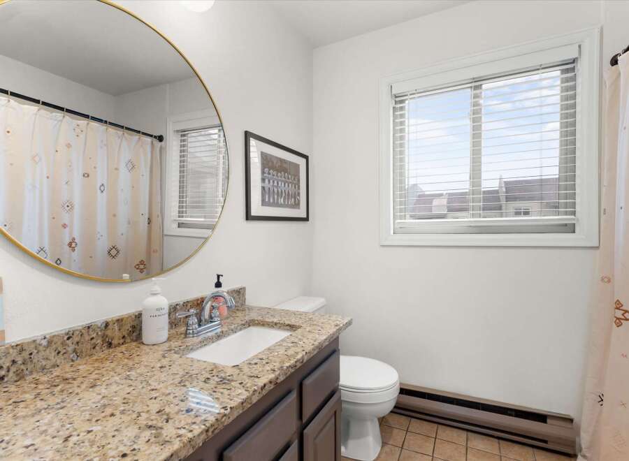 This bathroom features a stylish round mirror, a granite countertop, and a modern sink.
