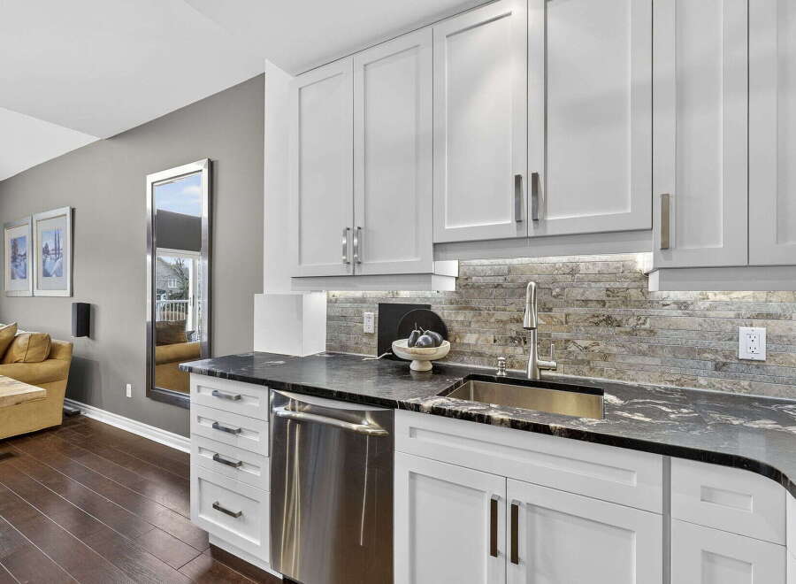 This stunning kitchen boasts sleek white cabinetry, a modern stainless steel dishwasher, and a beautiful granite countertop.