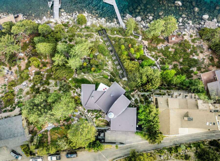 Experience luxury living with this stunning aerial view of a modern architectural masterpiece nestled amidst lush greenery and overlooking crystal-clear waters.
