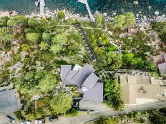 Experience luxury living with this stunning aerial view of a modern architectural masterpiece nestled amidst lush greenery and overlooking crystal-clear waters.