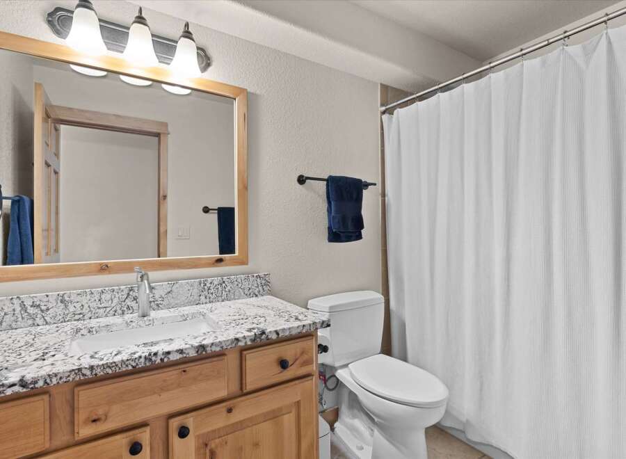 This beautiful bathroom features a stunning granite countertop and a stylish wooden vanity, offering both elegance and functionality.