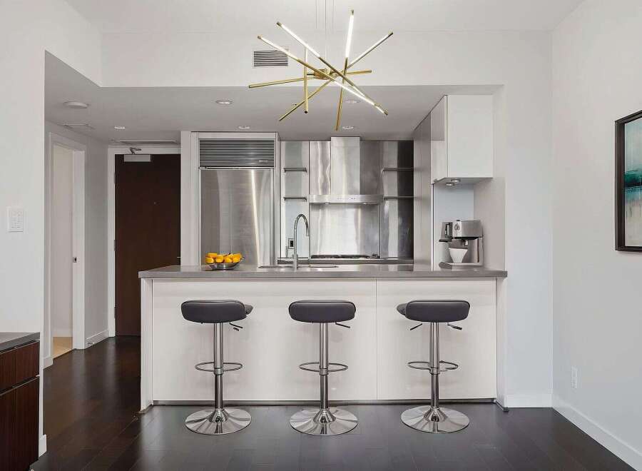 This modern kitchen boasts sleek stainless steel appliances, a stylish breakfast bar with three stools, and a contemporary chandelier.