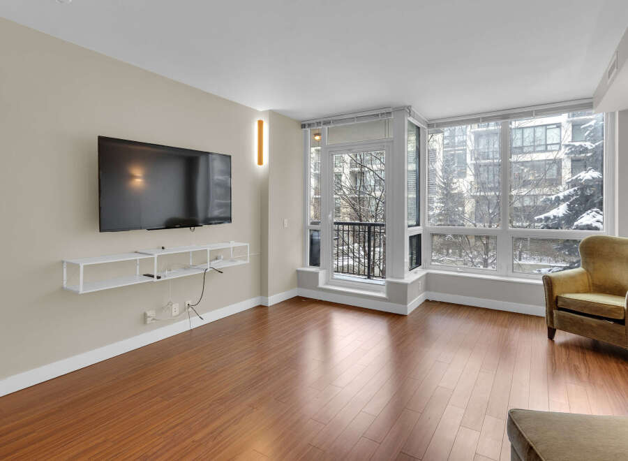 Experience modern living in this stunning condo featuring a spacious living area with a large flat-screen TV and a sleek, floating shelf.