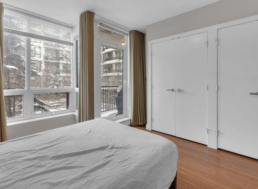 This bright and airy bedroom features a large window with a view of the surrounding neighborhood.