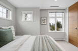 This bedroom offers a serene retreat with its neutral color palette and ample natural light.