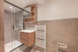 This modern bathroom features a sleek glass shower enclosure, a stylish wooden vanity with a sink, and a convenient towel warmer.