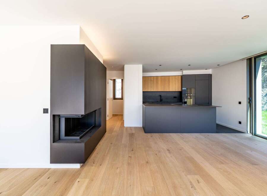 This modern living space features a sleek, dark gray fireplace and a contemporary kitchen with wooden cabinets.