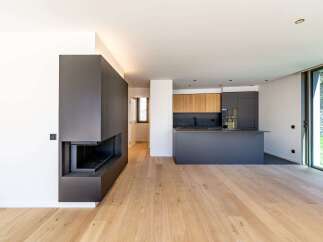 This modern living space features a sleek, dark gray fireplace and a contemporary kitchen with wooden cabinets.