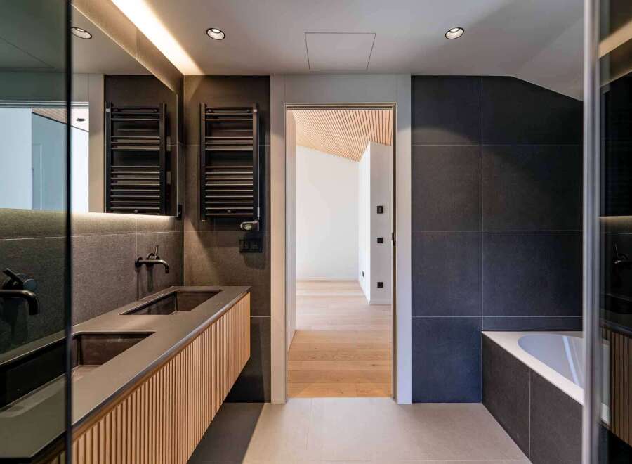 This modern bathroom showcases a sleek design with dark gray tiles and a wooden vanity.