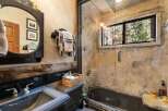 This rustic bathroom features a unique stone-like wall design and a dark-colored bathtub, creating a cozy and inviting atmosphere.