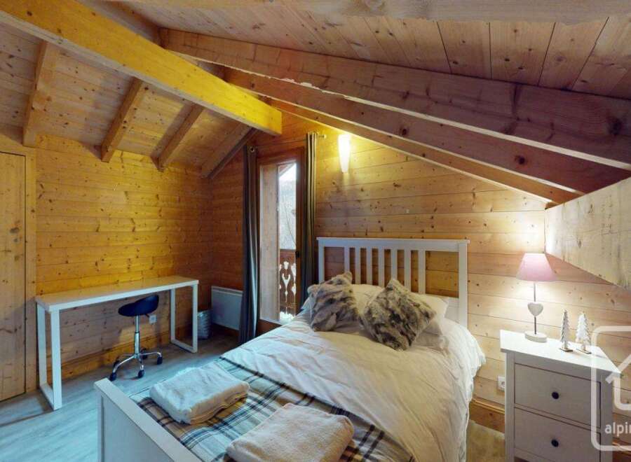This charming bedroom features a cozy, rustic design with wooden walls and a sloped ceiling, creating a warm and inviting atmosphere.