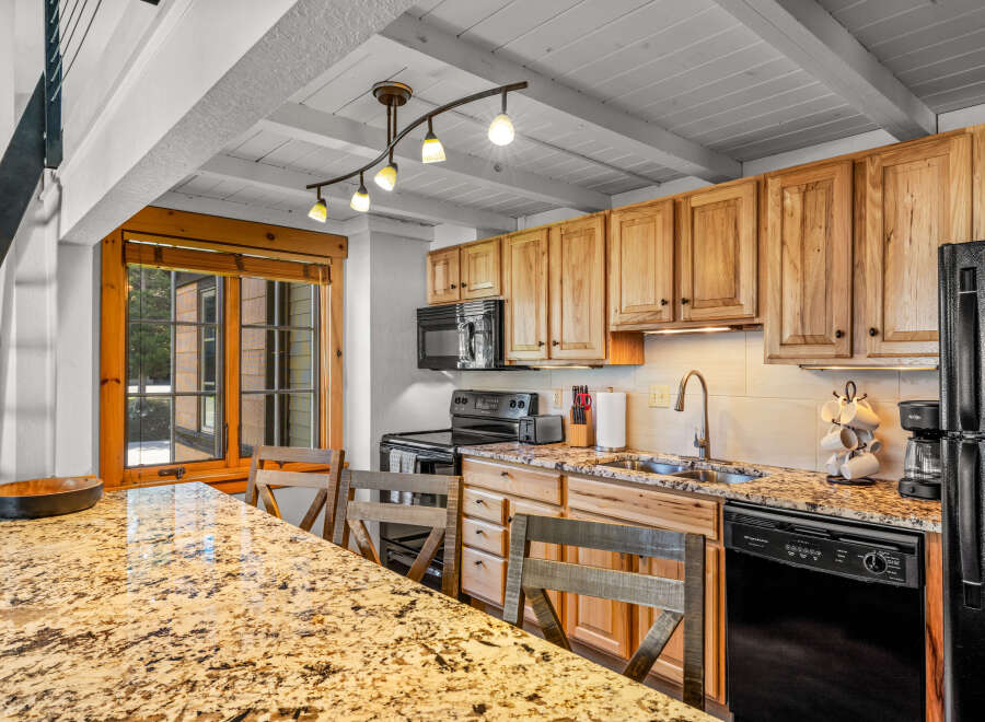 This stunning kitchen boasts beautiful wooden cabinetry, a sleek black appliance suite, and a gorgeous granite countertop.