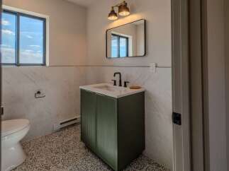 This stunning bathroom features a modern design with a sleek green vanity and a stylish black faucet.