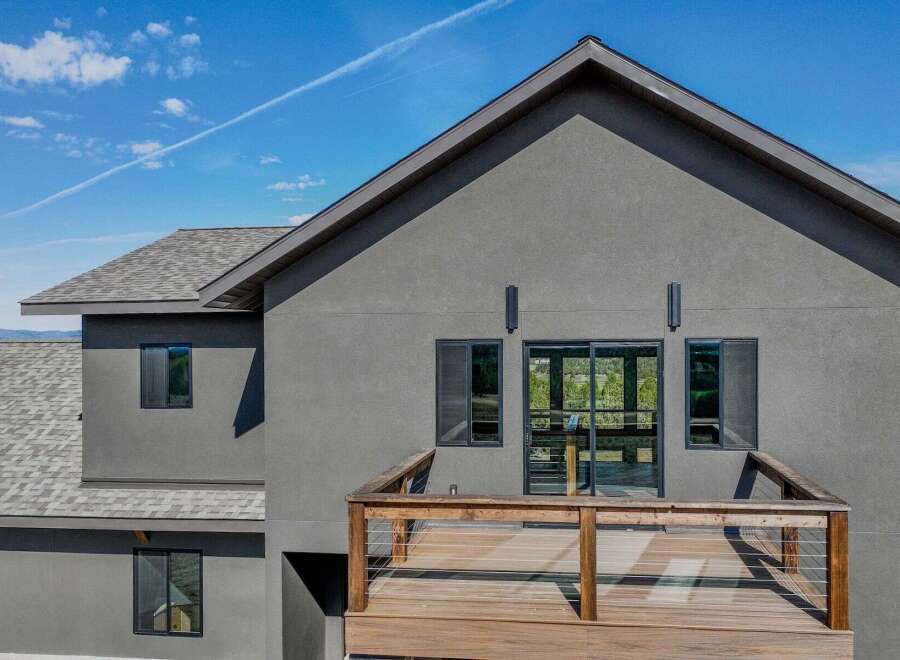This stunning modern home boasts a sleek, gray exterior and a spacious wooden deck, perfect for enjoying the outdoors.