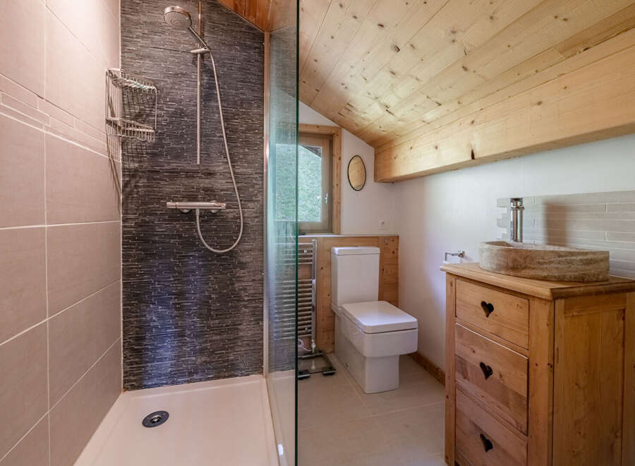 This charming bathroom features a rustic wooden vanity with a stone sink, adding a touch of natural elegance.