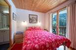 Discover the charm of this cozy bedroom, featuring a vibrant red floral bedspread and a wooden ceiling that adds warmth to the space.