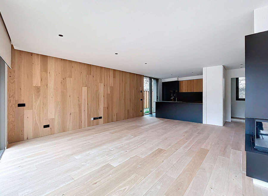 This stunning modern home features a spacious open-plan living area with beautiful light wood flooring and a feature wood-paneled wall.