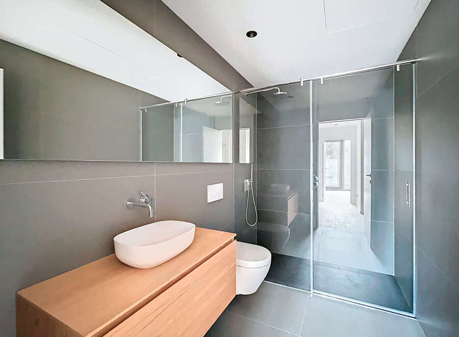 This modern bathroom features a sleek design with a glass shower enclosure and a floating wooden vanity.