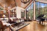 This stunning property boasts a luxurious living room with a grand piano and expansive windows that offer breathtaking views of the surrounding nature.