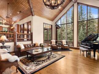 This stunning property boasts a luxurious living room with a grand piano and expansive windows that offer breathtaking views of the surrounding nature.