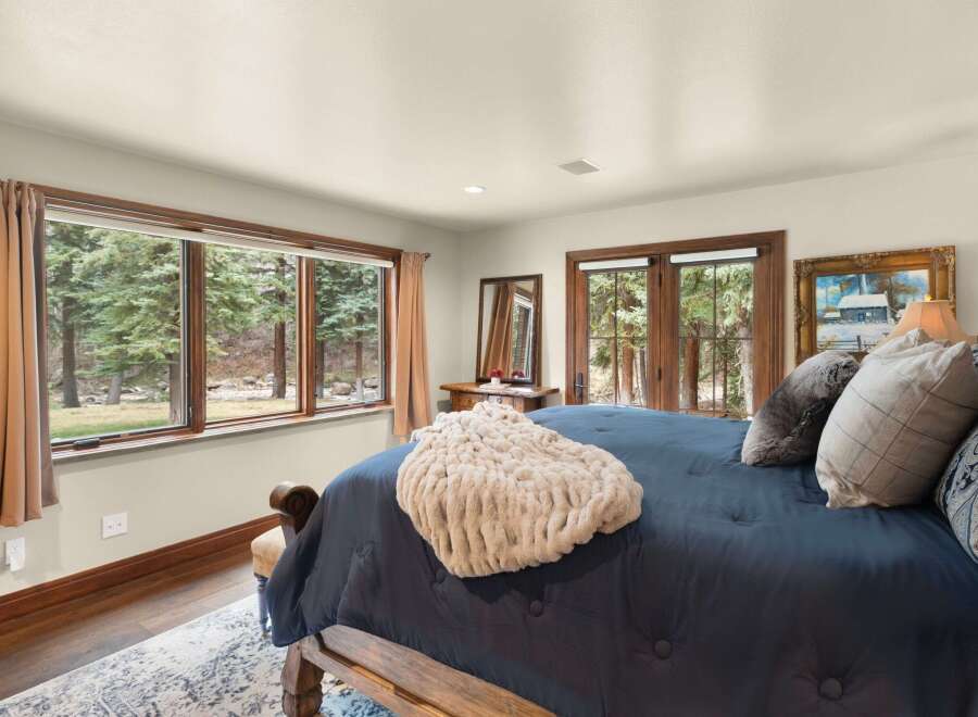 This stunning bedroom boasts a serene ambiance with its large windows offering picturesque views of the surrounding nature.