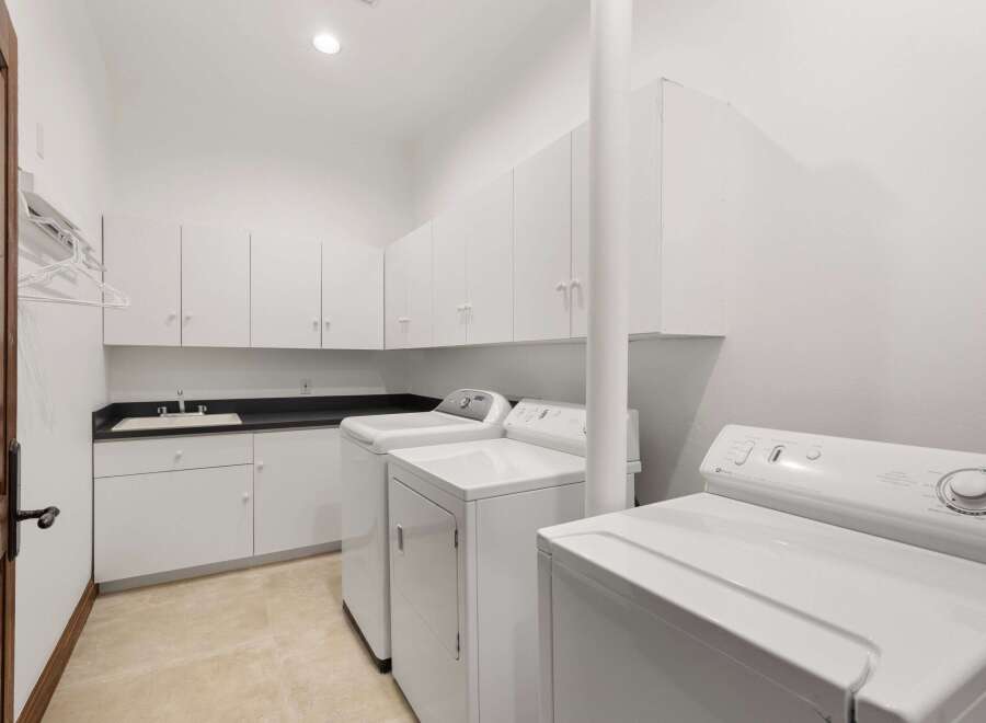 This stunning laundry room boasts ample storage with its sleek white cabinetry, perfect for keeping your space organized.