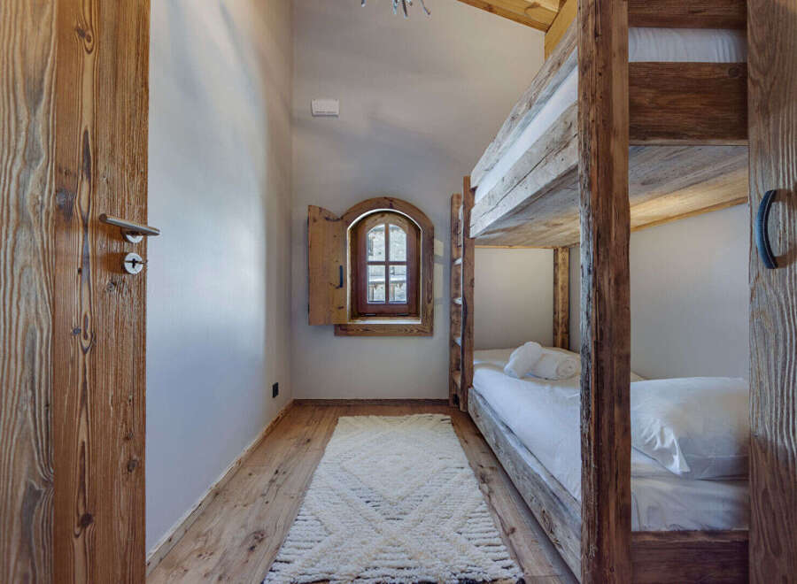 Discover the charm of this cozy bedroom featuring rustic wooden bunk beds and a unique arched window.