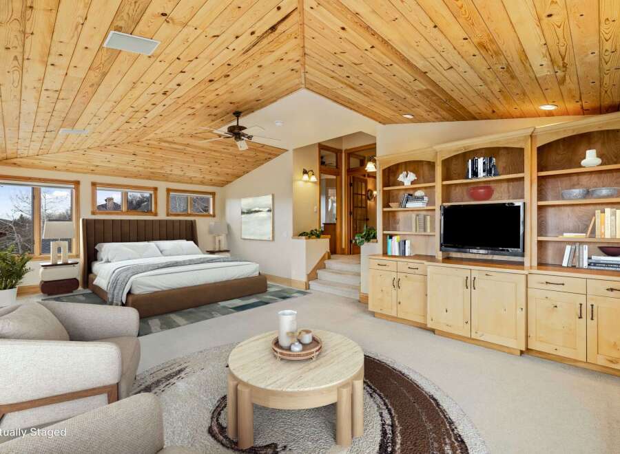 Experience luxury living in this stunning bedroom featuring a vaulted wood ceiling and a cozy seating area.