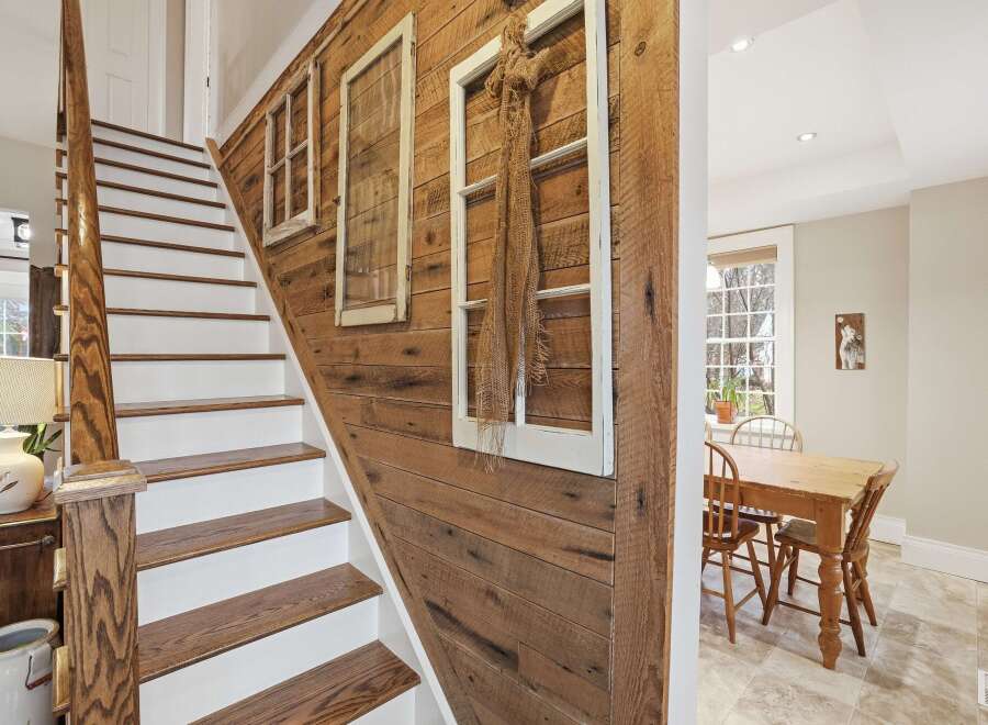 This charming home features a beautifully crafted staircase with wooden steps and white risers, complemented by a rustic wooden accent wall.