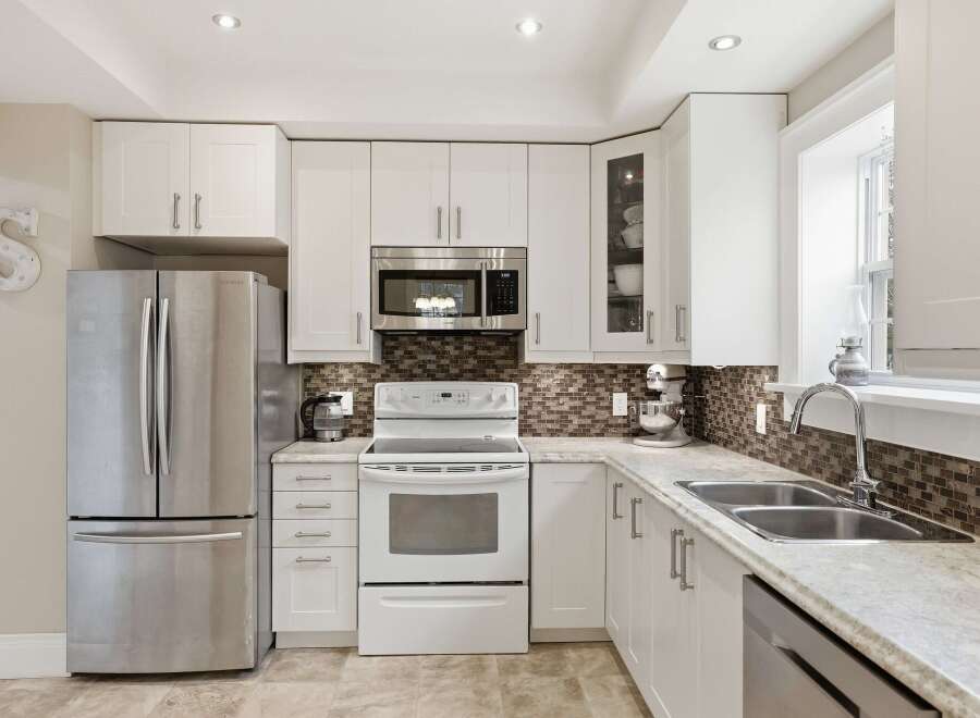 This stunning kitchen boasts modern white cabinetry, stainless steel appliances, and a beautiful backsplash.