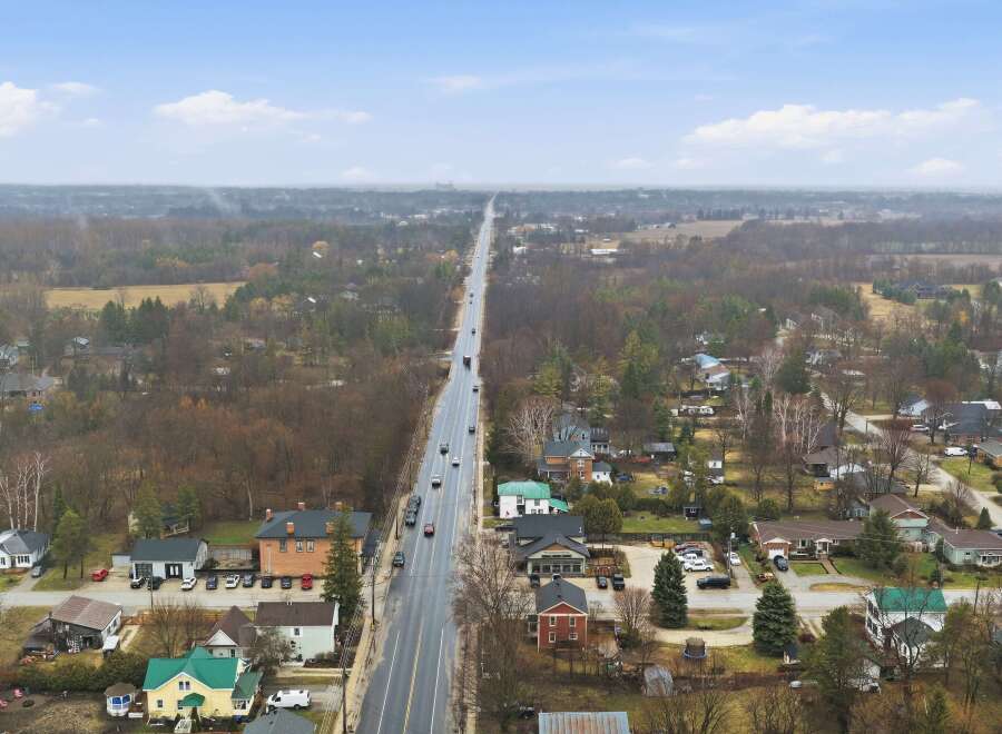 An aerial view showcases a charming town with a long road cutting through the center, lined with houses and businesses.