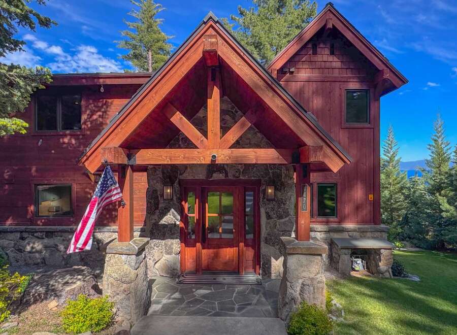 Experience luxury mountain living in this stunning timber-frame home, featuring a grand stone entryway and a welcoming wooden door.