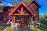 Experience luxury mountain living in this stunning timber-frame home, featuring a grand stone entryway and a welcoming wooden door.